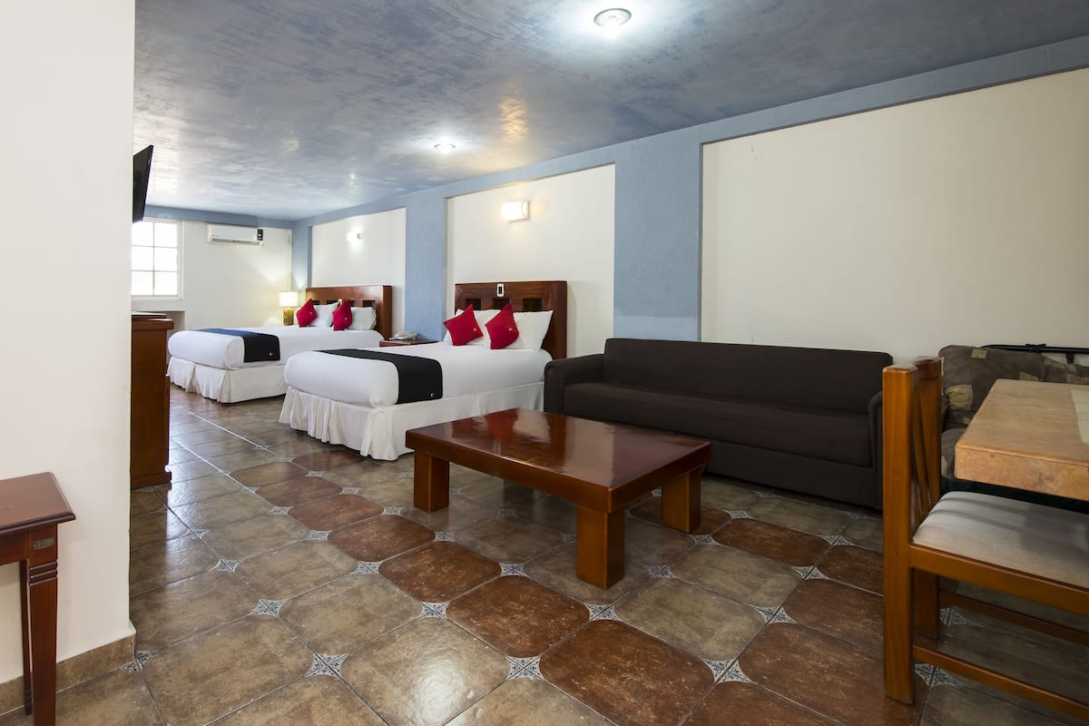 A hotel room with two beds, a sofa, a coffee table, and a TV.