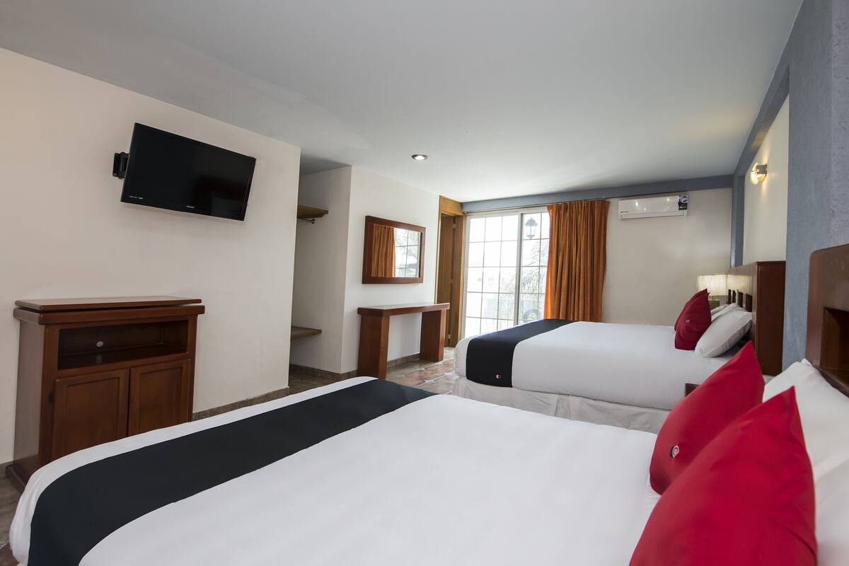 A hotel room with two beds, a television, a small table, and a window with curtains.