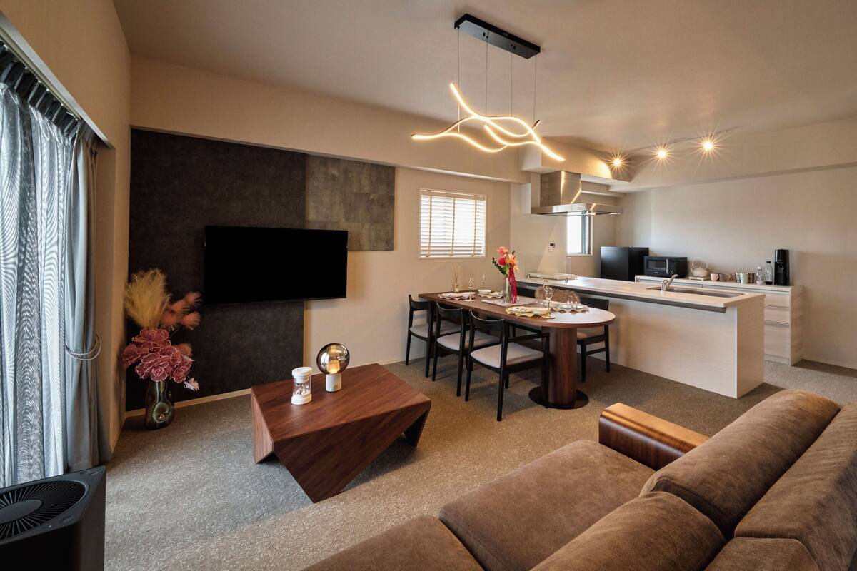 Una sala de estar moderna con sofá, una mesa de comedor con sillas, una zona de cocina con microondas y un televisor de pantalla plana montado en la pared.