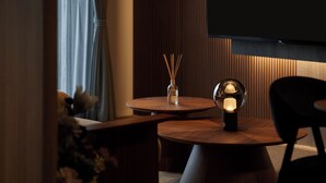 Une pièce moderne avec une table ronde en bois, une chaise noire, un flacon en verre contenant des tiges de roseau et une lampe sphérique.
