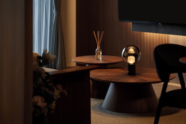 Une pièce moderne avec une table ronde en bois, une chaise noire, un flacon en verre contenant des tiges de roseau et une lampe sphérique.