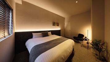 A hotel room with a bed, a chair, a small table, and a potted plant.