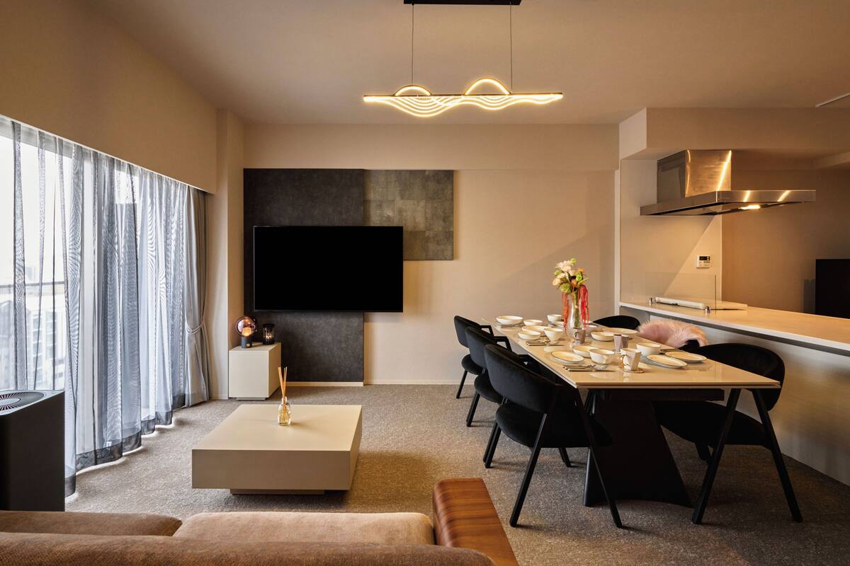 Una sala de estar moderna con un televisor de pantalla plana, un comedor con una mesa dispuesta para cuatro personas y un ventanal con cortinas traslúcidas.