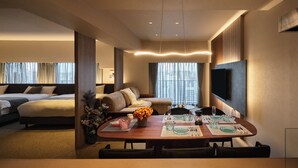 Une chambre d’hôtel comprenant un coin repas, un canapé, un téléviseur fixé au mur et une grande fenêtre avec des rideaux.