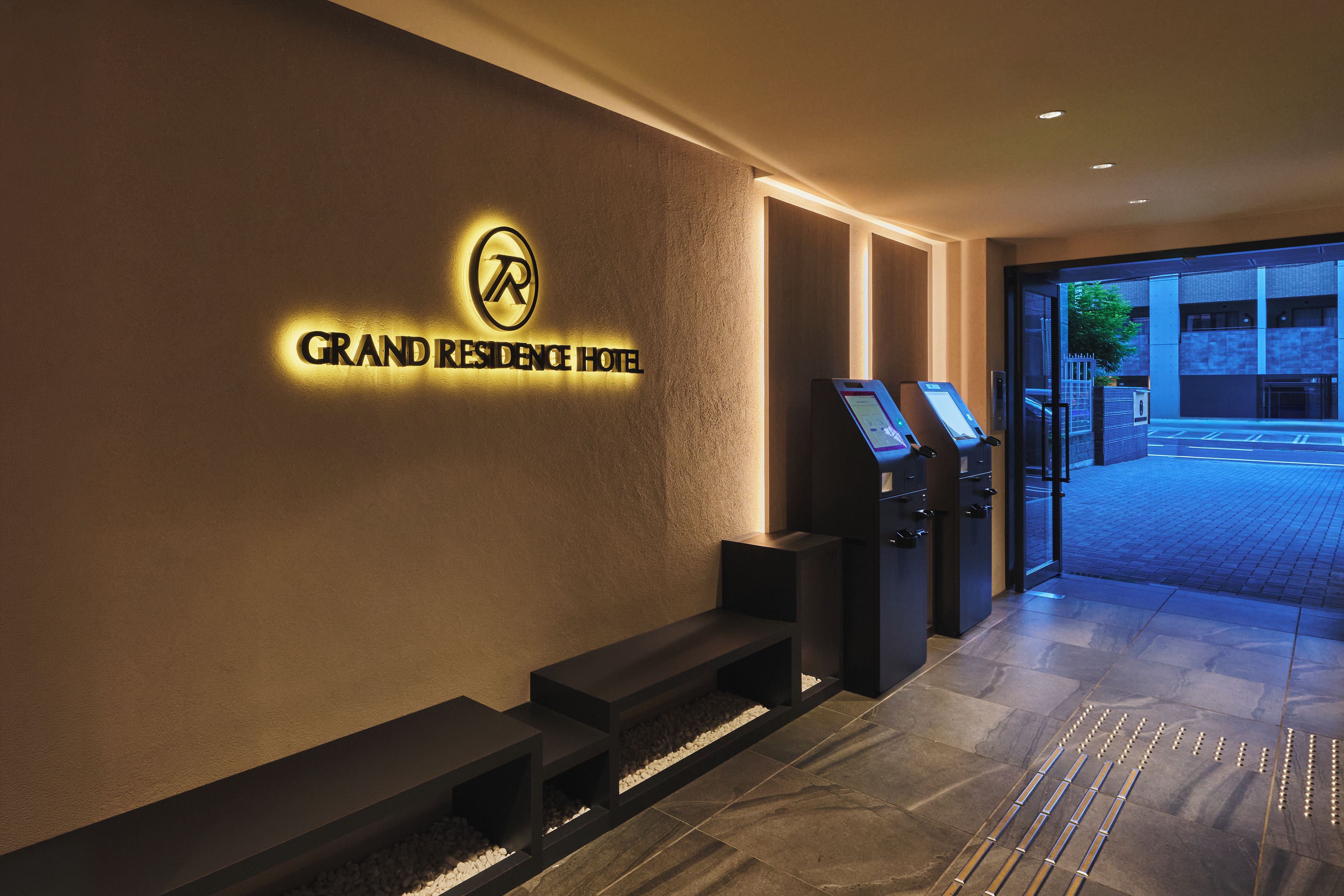 Een hotelentree met een receptiebalie, een digitale incheckkiosk en een bord met de naam Grand Residence Hotel.