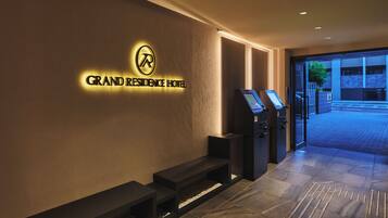 Een hotelentree met een receptiebalie, een digitale incheckkiosk en een bord met de naam Grand Residence Hotel.