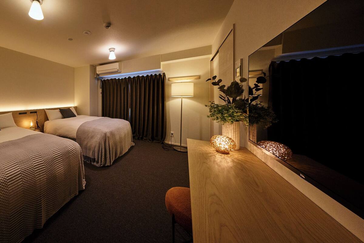 Habitación de hotel con dos camas, un escritorio con lámpara, un espejo y una planta.