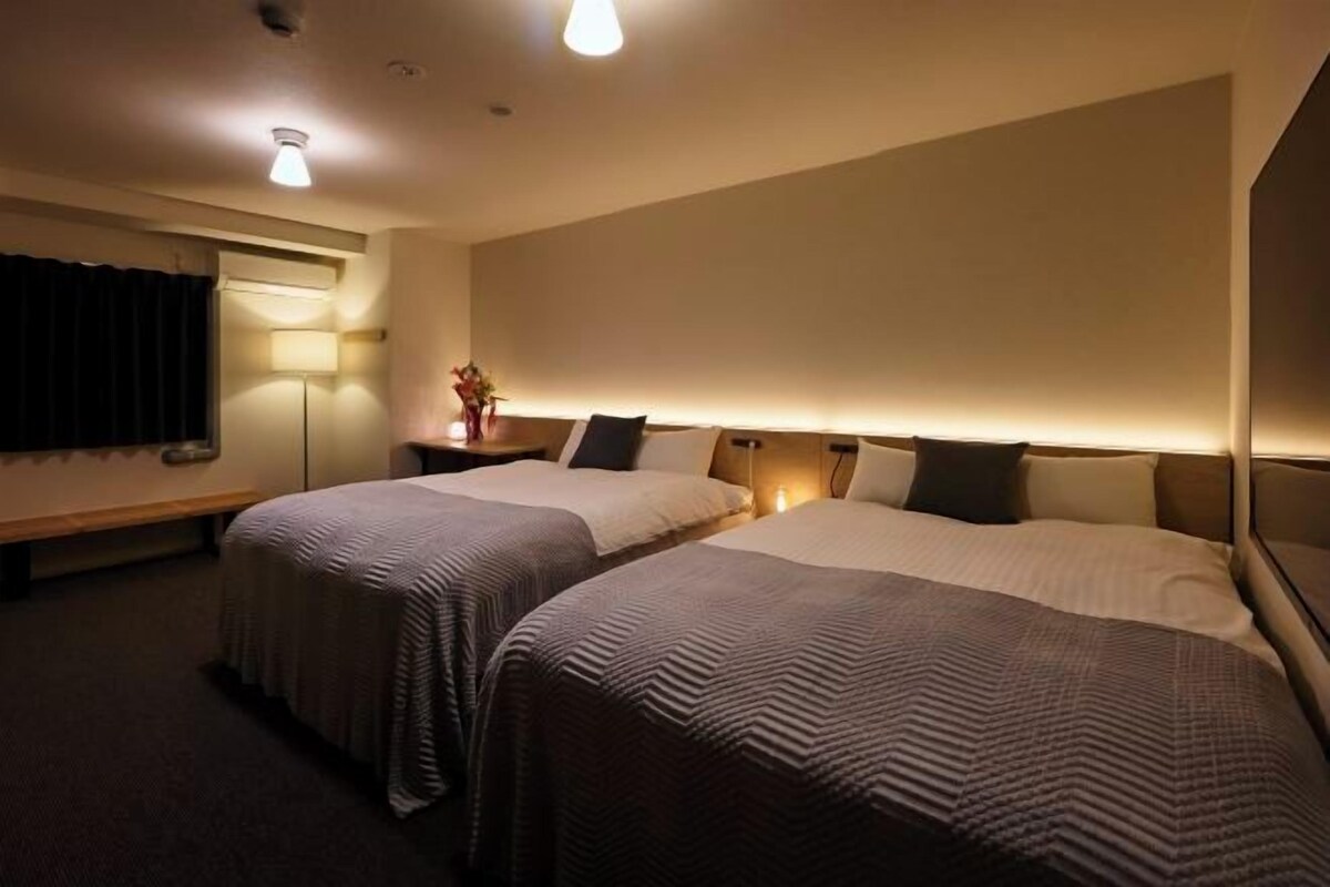 Une chambre d’hôtel avec deux lits, une table de chevet, une lampe et un banc.