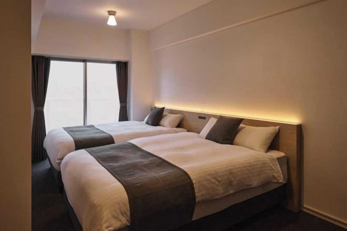 Ein Hotelzimmer mit zwei Betten, einem großen Fenster und einer Deckenleuchte.