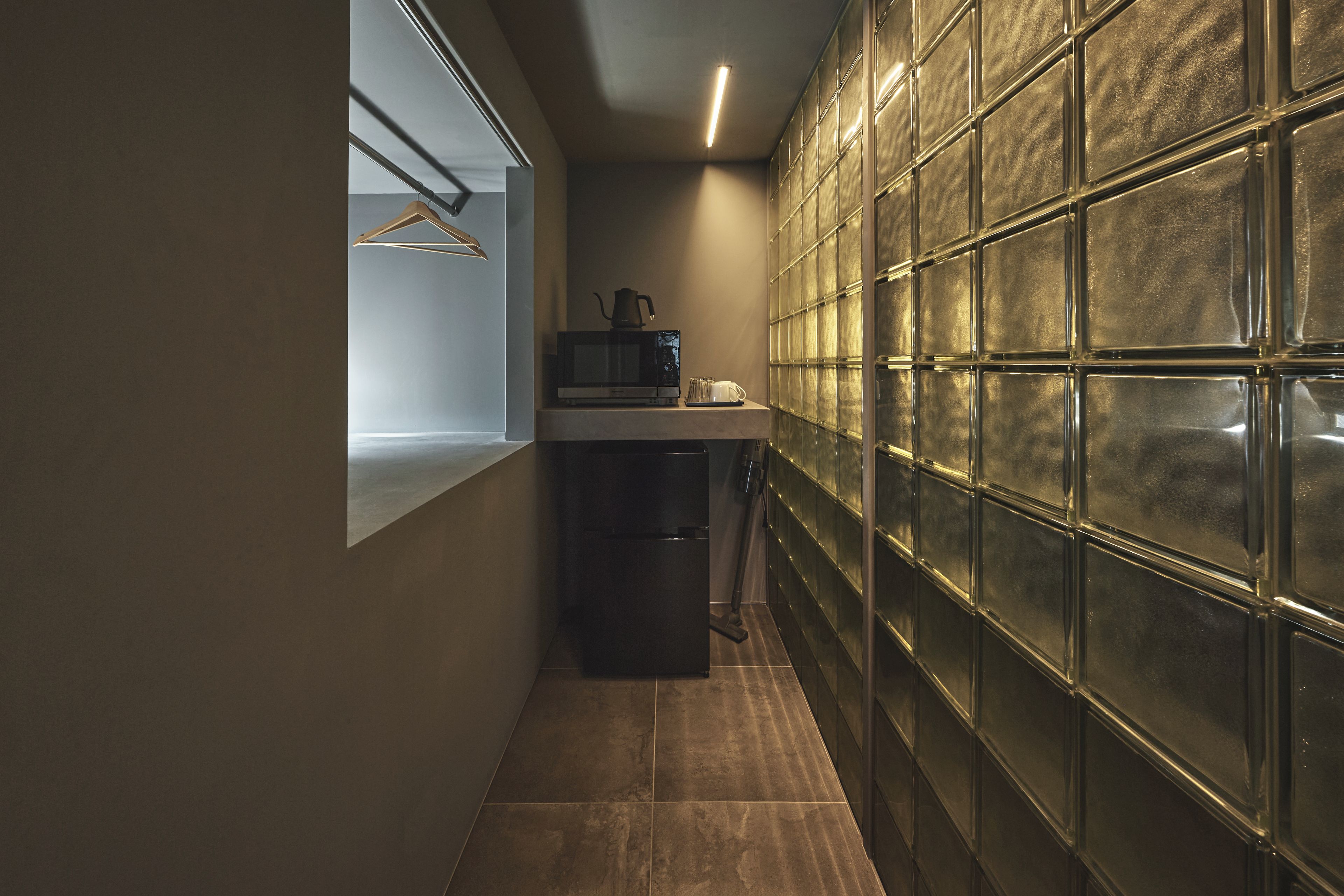 A narrow hallway with a microwave and a kettle on a counter, a hanging coat rack, and a tiled floor.