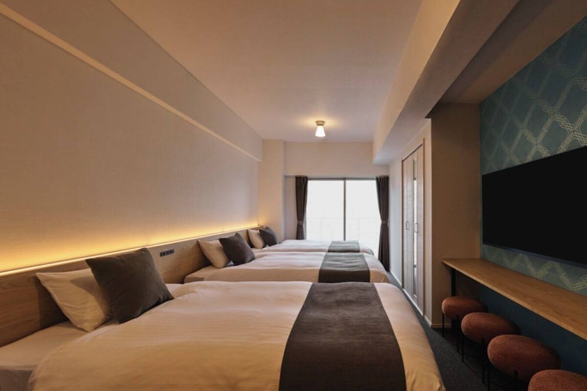 Habitación de hotel con tres camas, televisión y un ventanal grande.