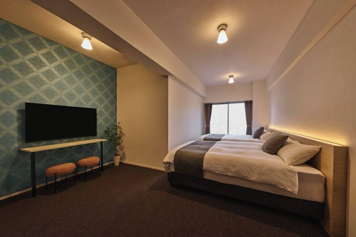 Habitación de hotel con cama, televisión, escritorio y dos sillas, además de un ventanal grande.