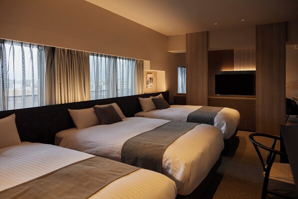 A hotel room with three beds, a flat-screen TV, and a desk with a chair.