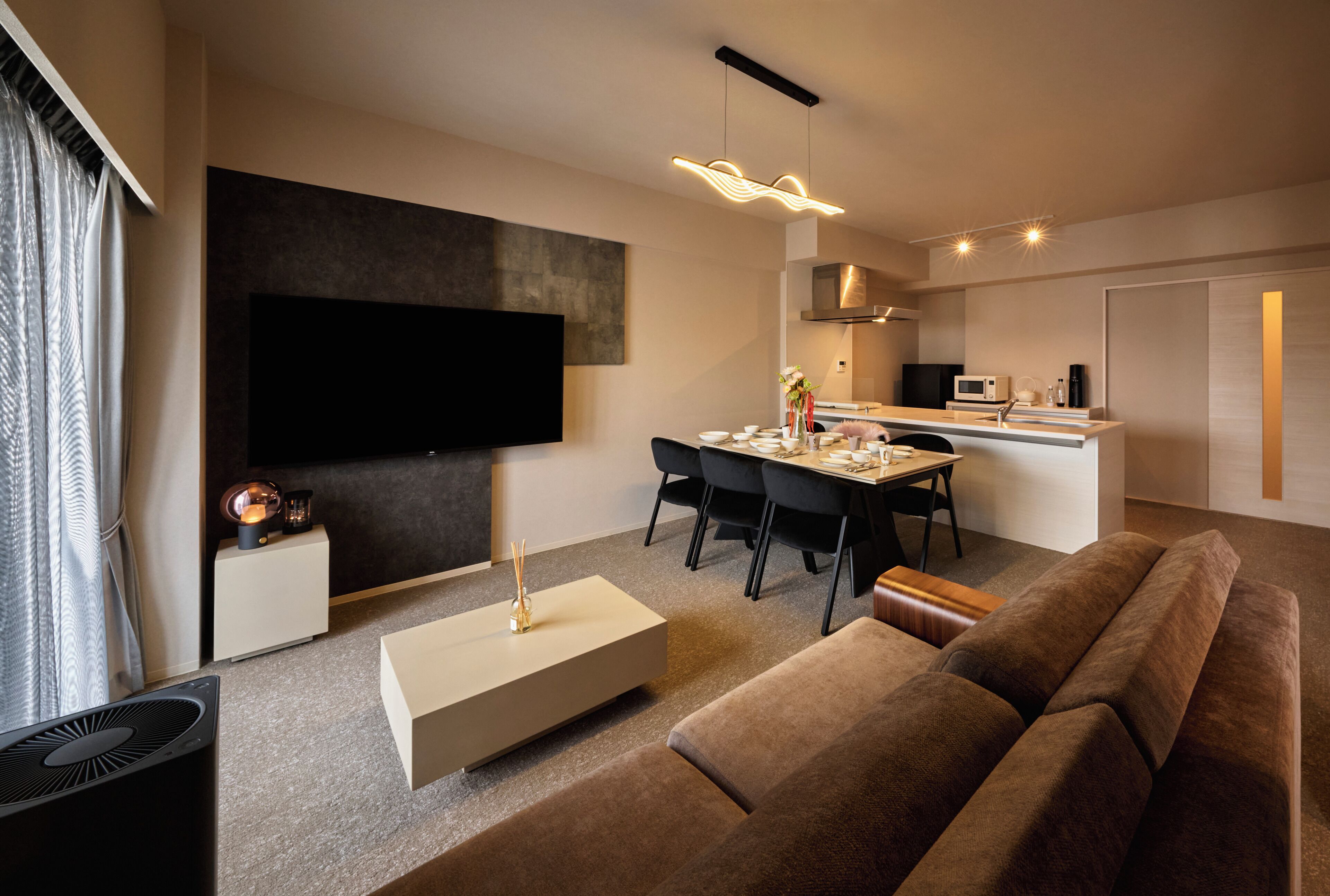 A modern living room with a flat-screen TV, a dining area, and a kitchen.