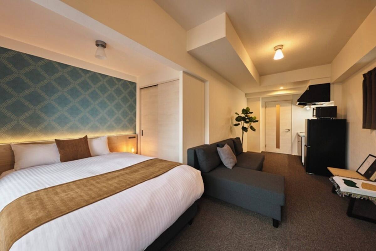 Una habitación de hotel con una cama grande, un sofá, un escritorio con computadora y un refrigerador.