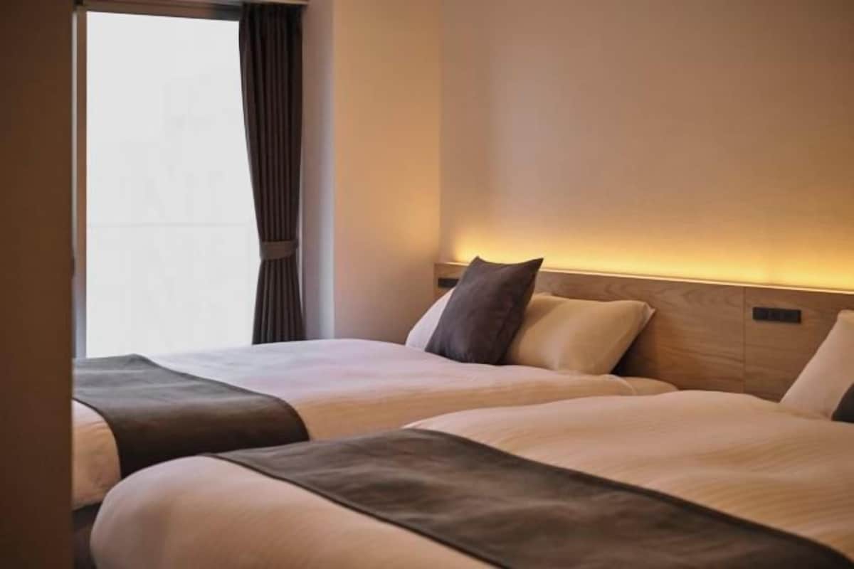 Una habitación de hotel con dos camas, una ventana con cortinas y una lámpara fijada a la pared.