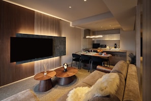 Un salon moderne doté d’un téléviseur à écran plat, d’une table basse ronde en bois, d’un canapé et d’un coin repas avec des chaises et une table.