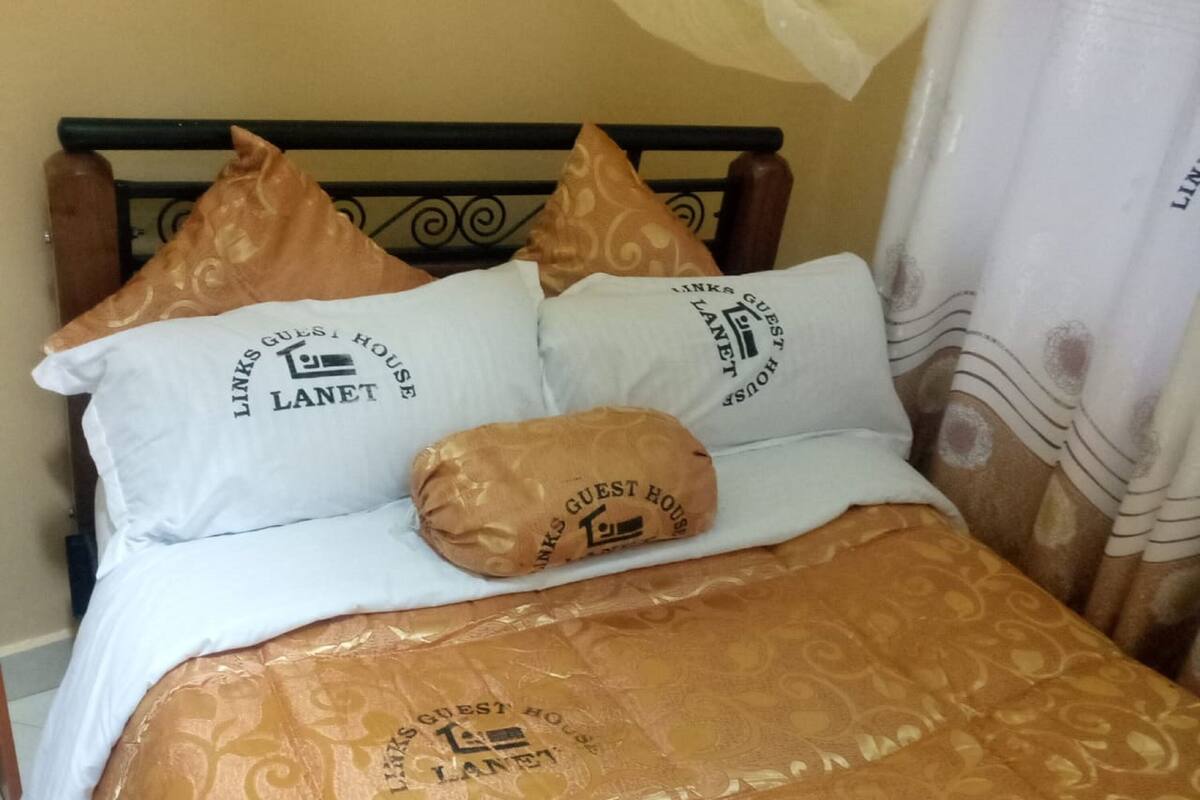 Una cama con una colcha estampada y almohadas con la marca 'LINKS GUEST HOUSE LANET'.