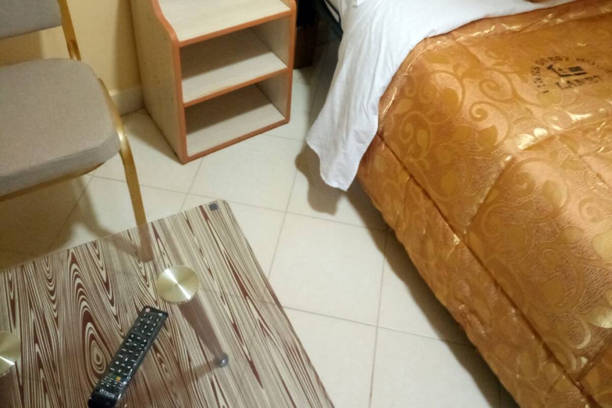 Una habitación de hotel con una cama, una mesita de noche de madera, una silla y un control remoto sobre una mesa de madera.