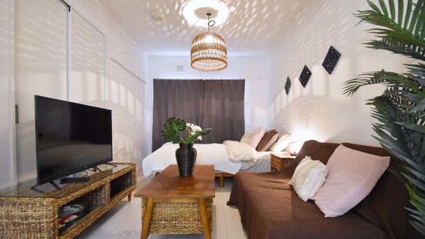 Ein modernes Wohnzimmer mit einem Flachbildfernseher auf einem Korpus-TV-Möbel, einem Holztisch, einem braunen Sofa und einer großen Pflanze.