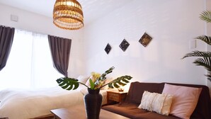 Ein modernes Schlafzimmer mit einem Bett, einem Holztisch mit Blumenvase, einem braunen Sofa und einer hängenden Leuchte.