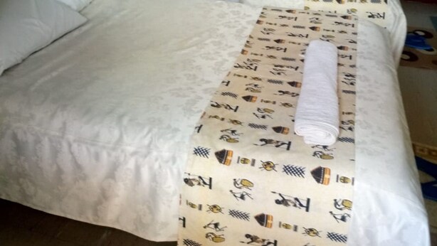 Een hotelkamer met twee bedden, wit beddengoed, een bedekt met een patroon, en een gordijn.