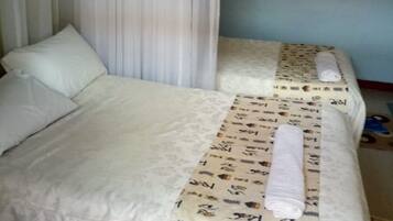 Habitación de hotel con dos camas, ropa de cama blanca, una manta estampada y una cortina.