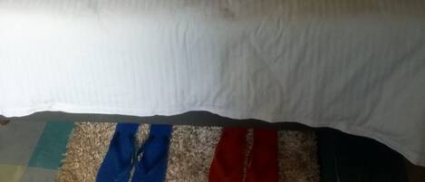 Una cama bien hecha con ropa blanca y dos almohadas, un cabecero y un tapete a rayas al pie de la cama.