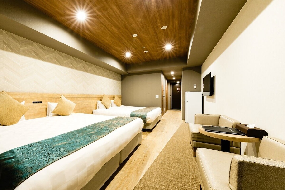 A hotel room with a large bed, a smaller bed, a desk, and a chair.