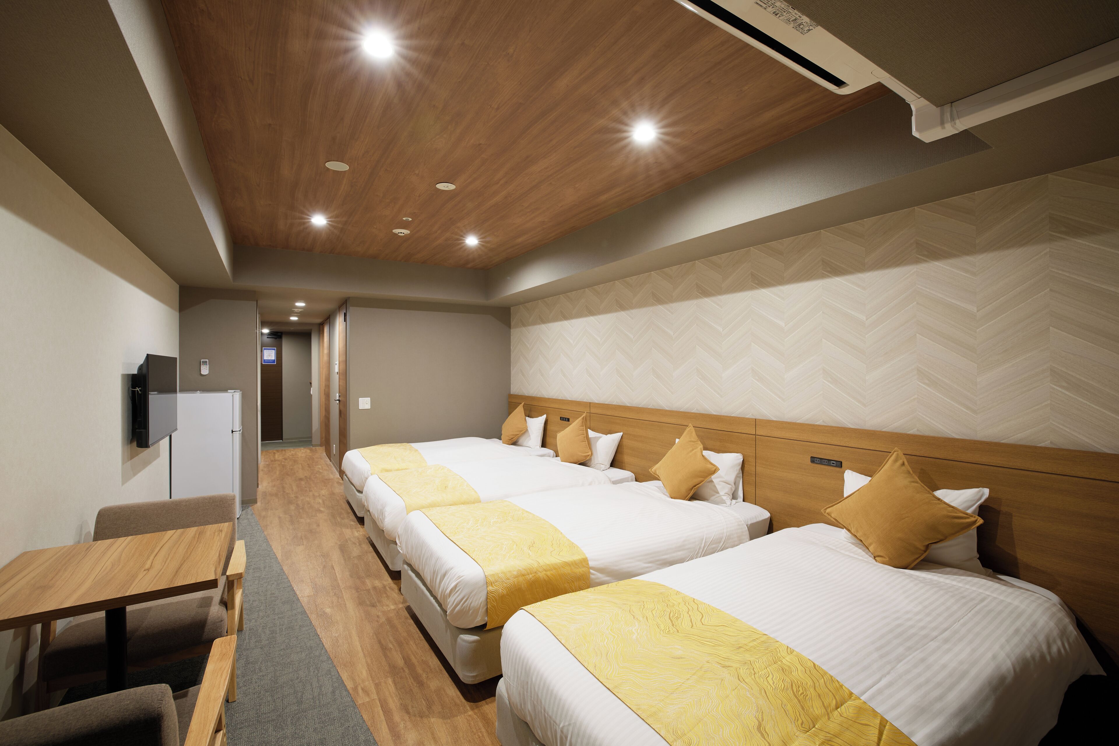 A hotel room with two beds, a desk, a television, and a corridor leading to another room.