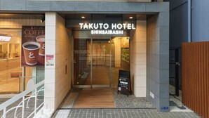 The exterior of Takuto Hotel Shinsaibashi with a glass entrance, signage, and a small signboard outside. - TAKUTO HOTEL Shinsaibashi (Osaka)