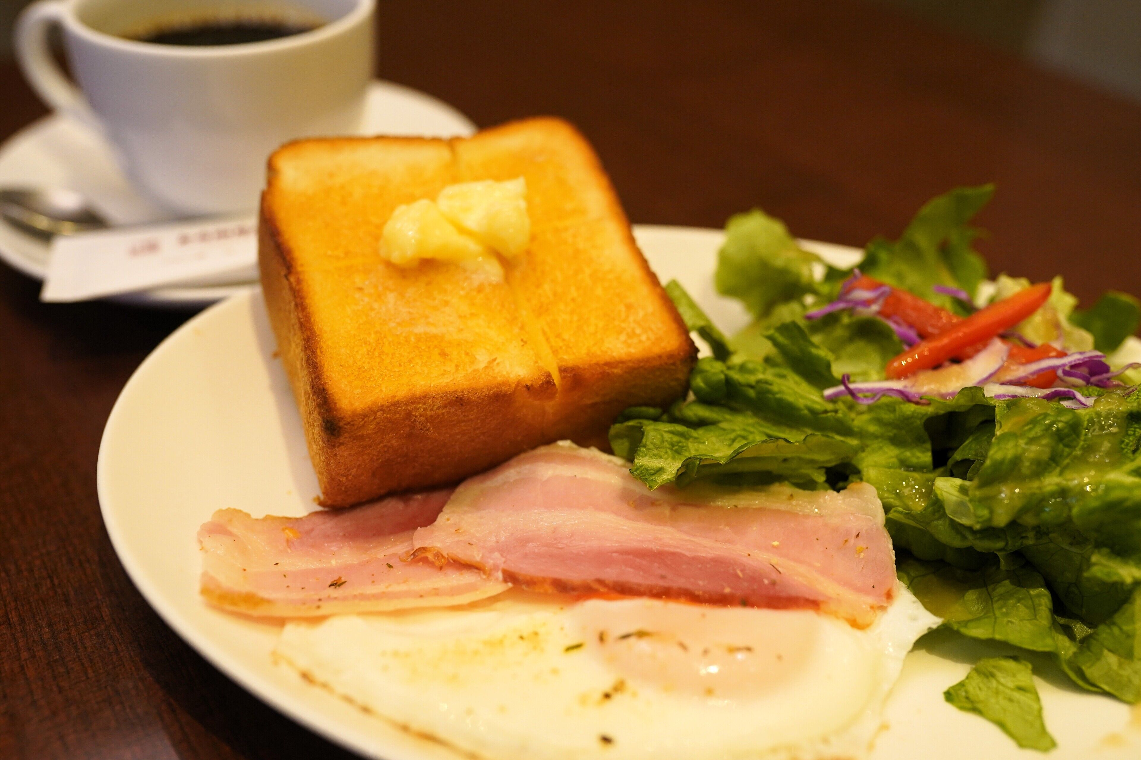 A plate with toast, bacon, an egg, and a salad.