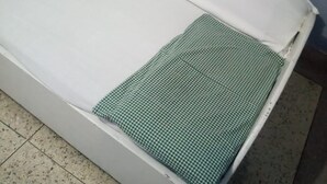 A partially assembled bed with a white mattress and a green checkered bedspread.