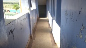 A corridor with peeling blue walls, a tiled floor, and a window at the end.