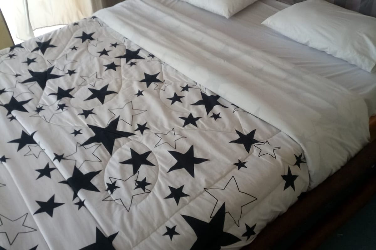 A bed with a white and black star-patterned bedspread, a wooden headboard, and a bedside table with a lamp.