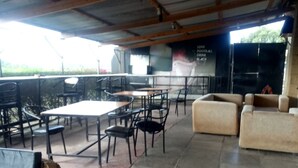 An outdoor seating area with tables and chairs, a cushioned sofa, and a wicker chair. - Hudson's Sports Bar and Restaurant (Nakuru)