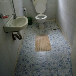 A small bathroom with a white sink, a toilet, and a green trash bin. The floor has a blue and white speckled tile pattern. - Hudson's Sports Bar and Restaurant (Nakuru)