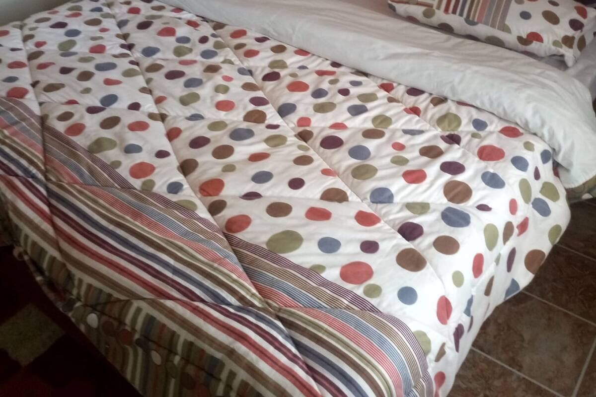 A bed with a polka dot and striped bedspread, a wooden headboard, and a bedside table with a lamp.