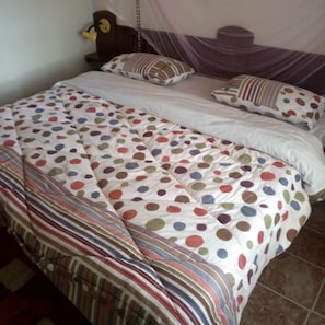 A bed with a polka dot and striped bedspread, a wooden headboard, and a bedside table with a lamp. - Hudson's Sports Bar and Restaurant (Nakuru)
