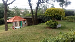 A grassy area with a small Coca-Cola branded tent, a neatly trimmed bush, and a wooden structure in the background. - Hudson's Sports Bar and Restaurant (Nakuru)
