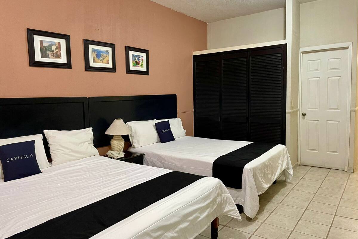 A hotel room with two beds, a nightstand, a lamp, and a door.