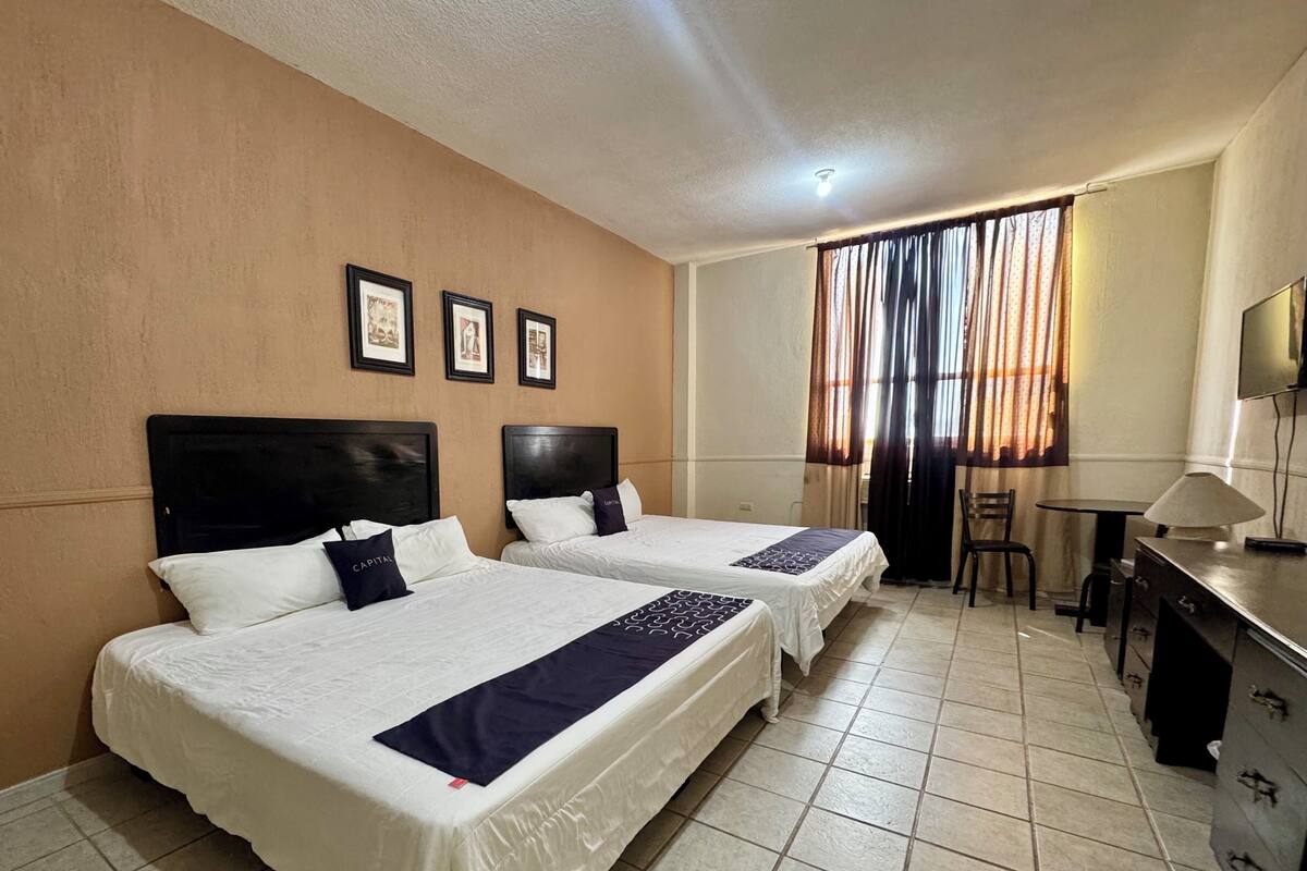 A hotel room with two beds, a desk, a chair, and a TV.
