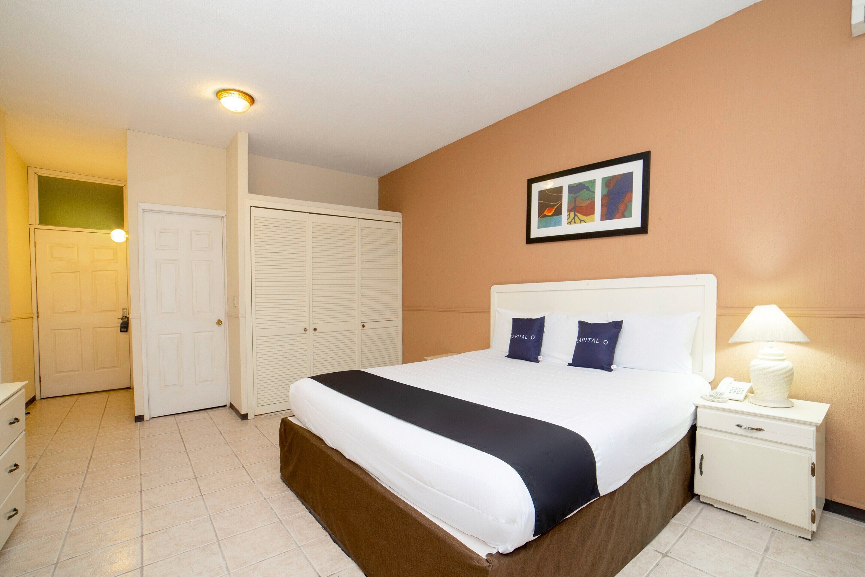 A hotel room with a bed, a nightstand with a lamp, a wardrobe, and a door leading to another room.