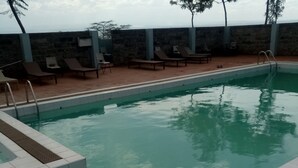 A swimming pool with lounge chairs and a stone wall in the background. - Top Cliff (Nakuru)
