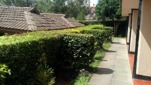 A pathway flanked by neatly trimmed hedges and a building with a tiled roof. - Top Cliff (Nakuru)