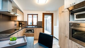 A modern kitchen with a black countertop, wooden cabinets, a built-in oven, and a window overlooking a street. - Holiday Home in Frasnes With Garden (Couvin)