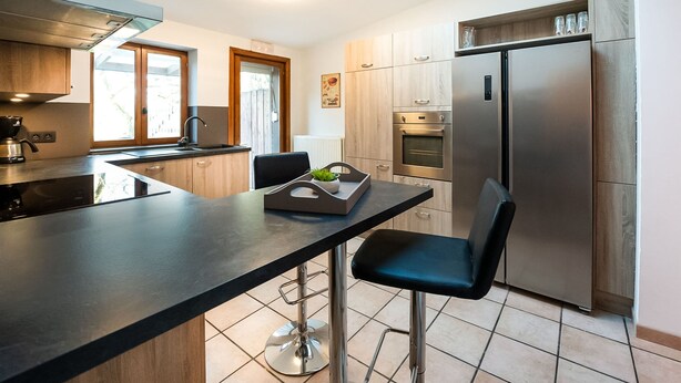 A modern kitchen with a central island, bar stools, stainless steel appliances, and wooden cabinetry. - Holiday Home in Frasnes With Garden (Couvin)
