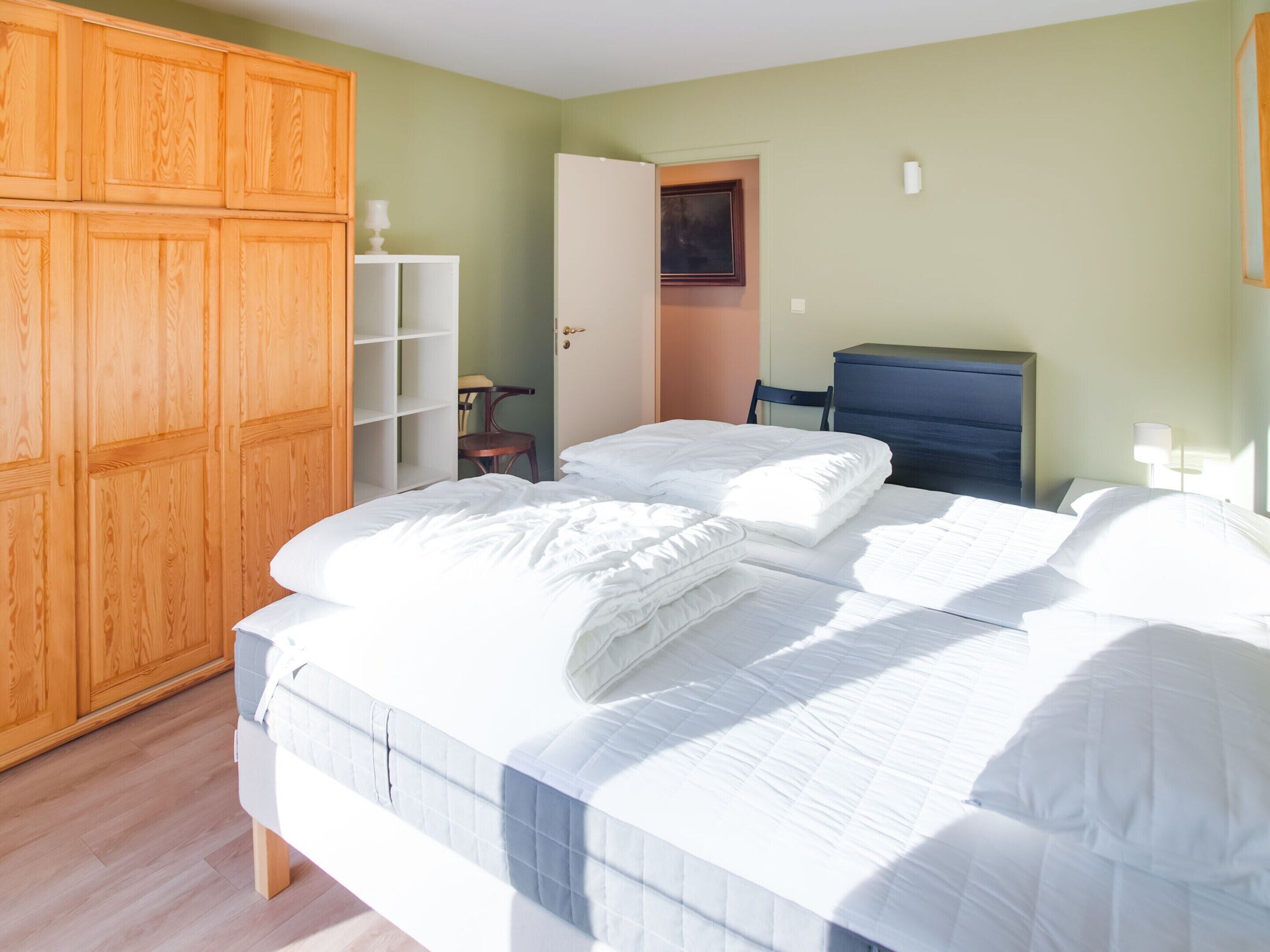 A bedroom with a large bed, wooden wardrobe, and a desk.