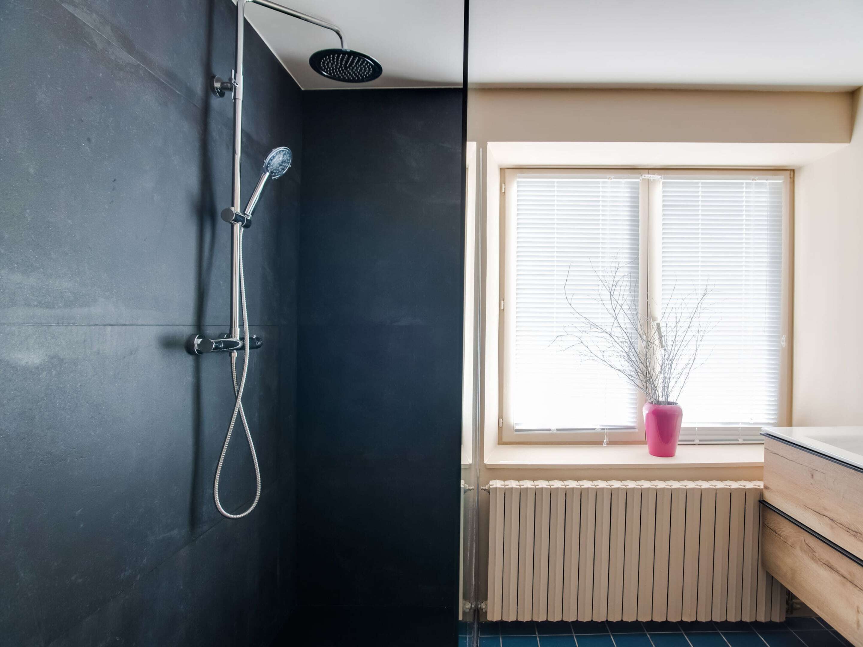 Ein Badezimmer mit Dusche, einem Fenster mit Jalousien und einem Heizkörper.