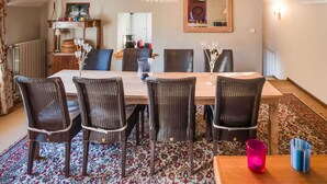 A dining area with a wooden table, wicker chairs, a chandelier, and a patterned rug. - Luxury Pool Villa in Sosoye (Anhée)